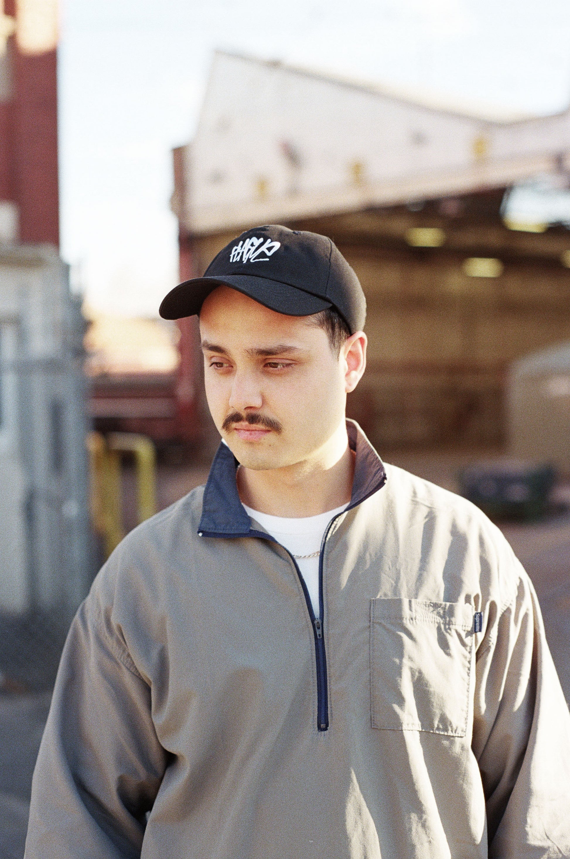 Man wearing a cap and beige jacket in an outdoor setting